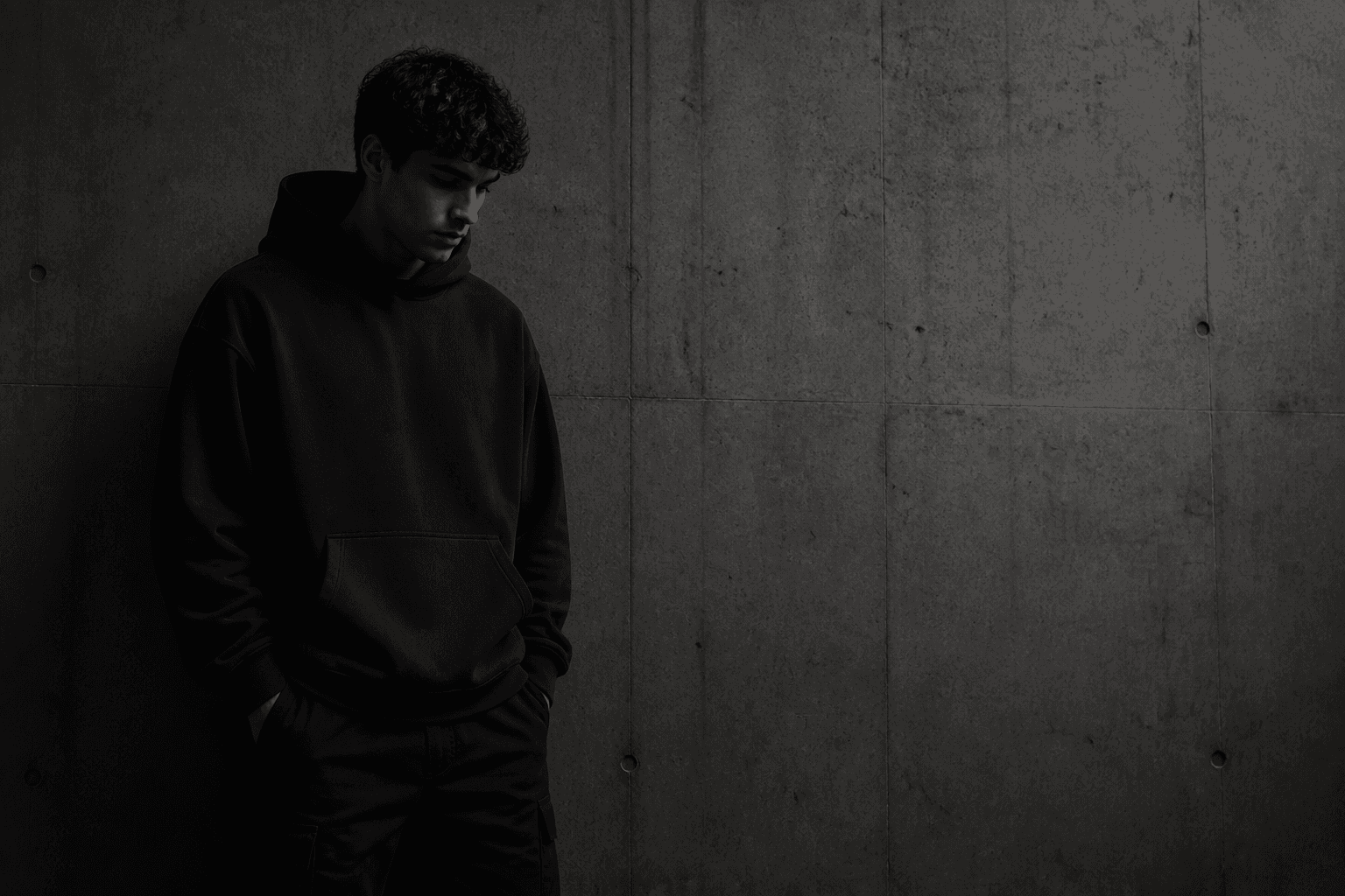 Model in a black hoodie standing against a concrete wall